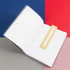 The Brass Bookmark Ruler inside of the book on a colorful background.