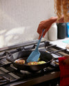 A hand holding the GIR Ultimate Slate Flip to flip patties on a frying pan.