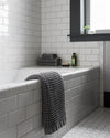 A Onsen Cinder Grey Bath Sheet hanging over a bath tub.