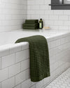 The Onsen Forest Waffle Bath Sheet hanging over a bath tub.