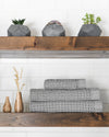 The Onsen Cinder Gray Waffle Bath Towel set on a wooden shelf.