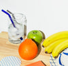A straw from the Glass Straws in Cool Set in a glass on ice water next to some fruit.