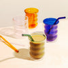 Different colored Double Wall Groovy Cup with straws, one filled with tea on a cream surface.