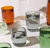 A side view of the different color and sizes of Century Glasses filled with water on a cream background.