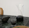 The Clear Pour Over Carafe and Clear Double Wall Glass filled with coffee on a marble countertop