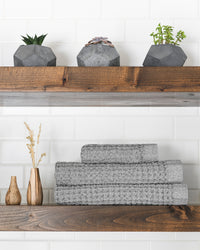 The Onsen Cinder Gray Waffle Bath Towel set on a wooden shelf.