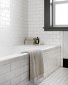 The Onsen Oatmeal Bath Towel over the edge of a bathtub.