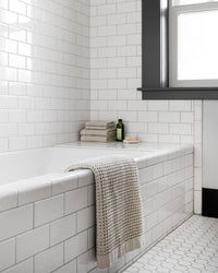 The Onsen Oatmeal Bath Towel over the edge of a bathtub.