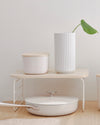The Small Cream Storage Bin with a wooden lid on a shelf riser.