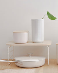 The Small Cream Storage Bin with a wooden lid on a shelf riser.