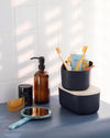 Small Navy Storages Bins with beauty products and one with a  wooden lid on top of each other on a cream background.