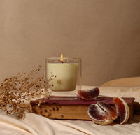 The 6 oz Double wall Candle displayed on on top of a book with Pomelo's on the right hand corner. 