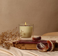 The 6 oz Double wall Candle displayed on on top of a book with Pomelo's on the right hand corner. 