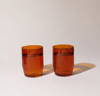 Two 12 oz Amber Century Glasses filled with water on a cream background. 